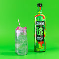 A bottle of Corky’s Sour Apple Schnapps with a green apple schnapps cocktail on a green background.