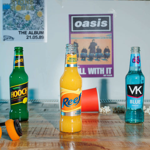 Showcasing the 90's party pack displaying a bottle of each Lemon Hooch, Reef Orange & Passionfruit and VK Blue. There is an Oasis Roll With It poster and The Stone Roses The Album poster referencing the 90's theme.