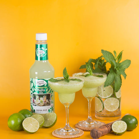 Bottle of Master of Mixes Mojito syrup with two cocktails and limes on a yellow background