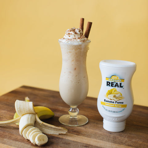 A banana milkshake made with Real banana syrup, with the bottle of Real next to it. 