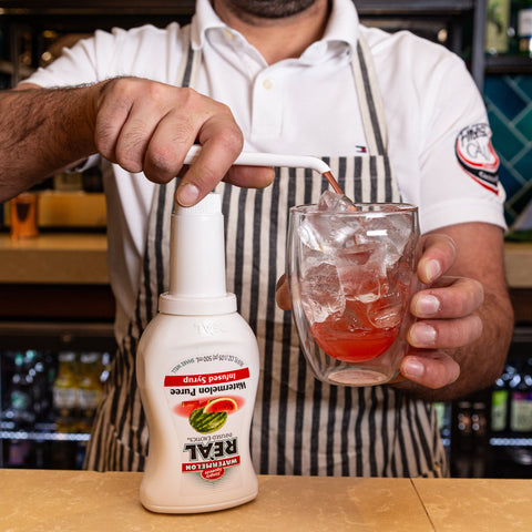 Someone squeezing Reál watermelon syrup into a glass, Reál syrups are perfect for cooking & baking, making cocktails or mocktails and dirty sodas. 