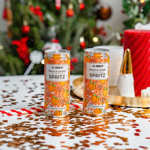 Two ready to drink cans of peach & lychee white wine spritz in a Christmas setting. 