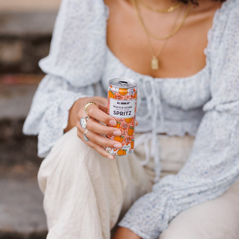 Someone holding a ready to drink can of All Shook Up peach and lychee white wine spritz. 