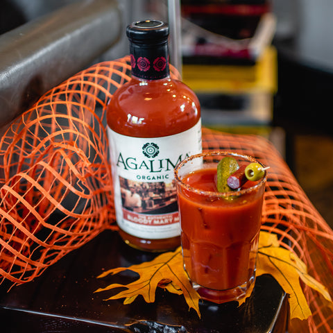 A 1L glass bottle of Agalima Organic Bloody Mary Mix next to a glass of bloody mary served with garnishes