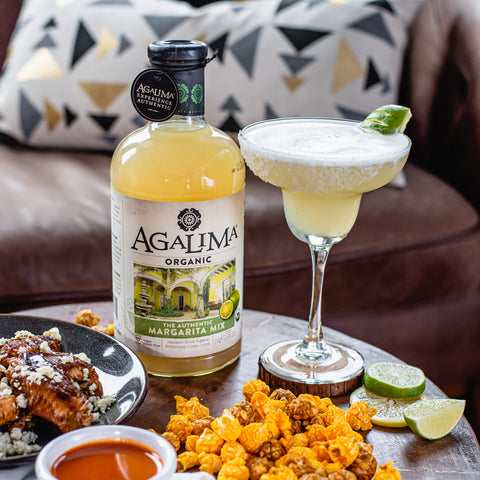 A 1L glass bottle of Agalima Organic Bloody Mary Mix next to a margarita cocktail with a salted rim.