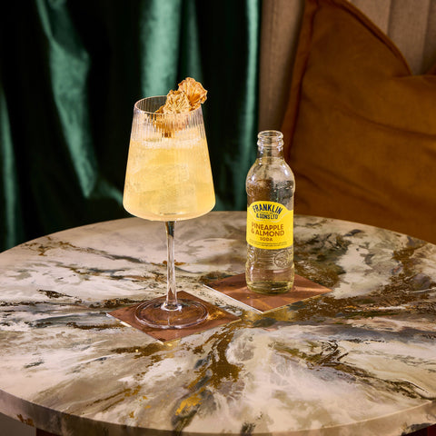 A bottle of Franklin & Sons pineapple & almond soda, being used as a premium mixer in the glass next to it. 