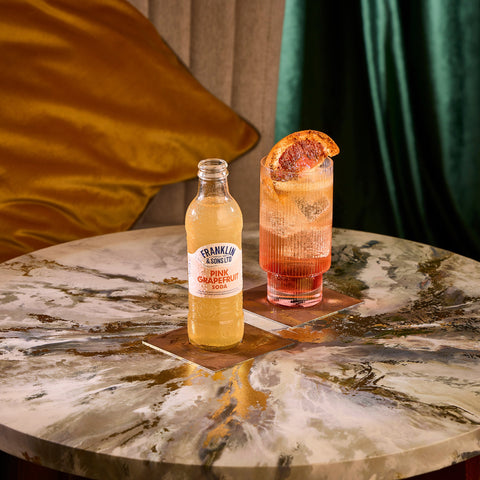 A bottle of Franklin & Sons pink grapefruit soda, next to a drink where the soda has been used as a premium mixer. 