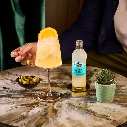 Someone sat at a table with a drink that has been made with Franklin & Sons premium Sicilian lemon tonic water.