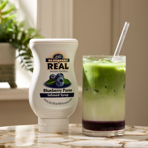 A blueberry matcha made using Reàl Blueberry Puree Infused Syrup with the bottle of Reàl next to the matcha. 