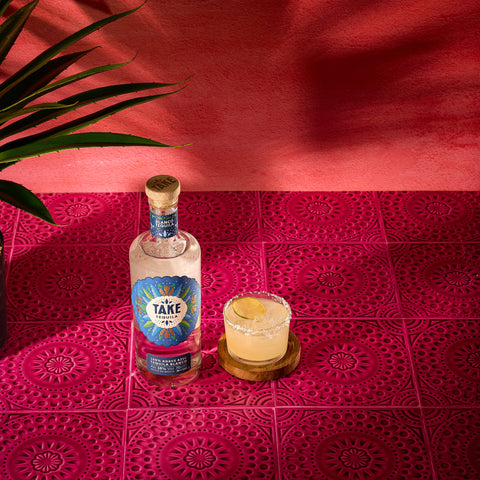 A bottle of Take Tequila Blanco, made with 100% agave azul, with a margarita cocktail next to the bottle.