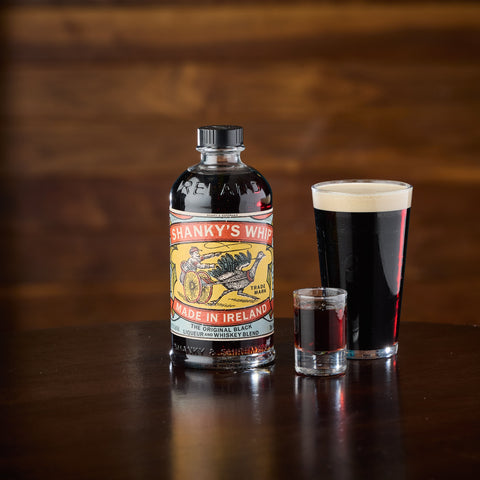 A bottle of Shanky's Whip Irish liqueur and whiskey blend next to a shot of Shanky's Whip and a pint of stout for the perfect drink pair. 