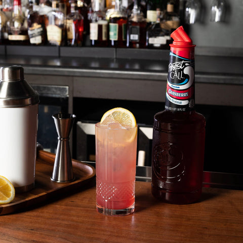 A cranberry cocktail made with Finest Call Premium Cranberry juice mix, with the Finest Call bottle placed behind the cocktail. 