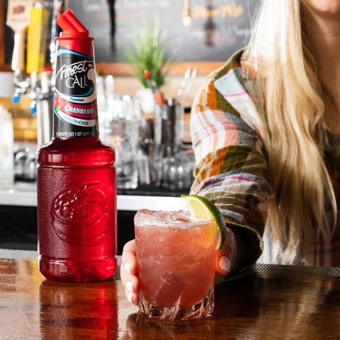 A cranberry cocktail made with Finest Call Premium Cranberry Juice with the Finest Call cocktail placed behind the cocktail. 