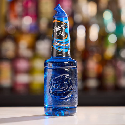 Blue bottle of Finest Call Blue Curacao on a bar counter with a blurred bar background