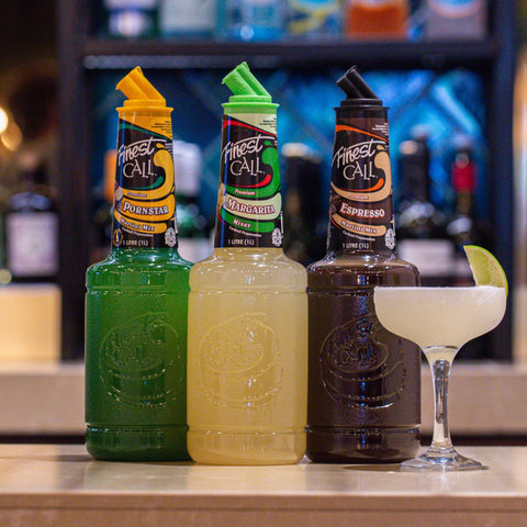 Three bottles of Finest Call Mixers in Pornstart Martini, Margarita, and Espresso Martini, with a cocktail glass on a bar counter.