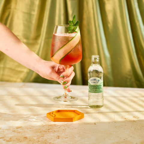Someone picking up a cocktail that's been  made using Franklin & Sons elderflower and cucumber tonic as a premium mixer. 