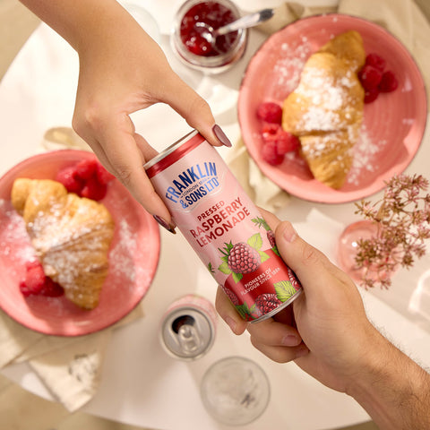 Two people holding a can of Franklin & Sons pressed raspberry lemonade, which is a premium soft drink. 