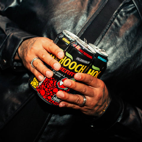 A person holding three cans of Hooch premixed and ready to drink alcopops. 