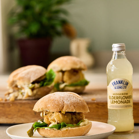 A bottle of Franklin & Sons hedgerow elderflower lemonade, a premium soft drink next to a burger. 