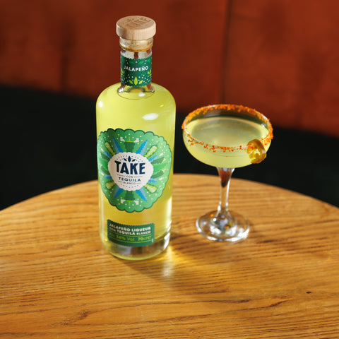 A bottle of Take jalapeno tequila liqueur next to a spicy margarita made with Take.