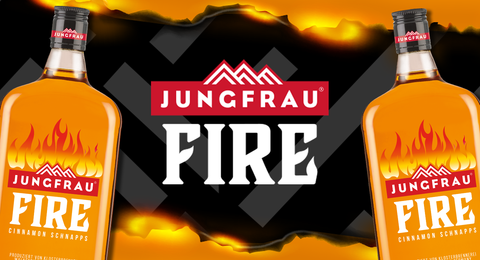 Jungfrau Fire Cinnamon Schnapps promotional banner featuring two bottles of Jungfrau Fire with a flame design against a dark mountain backdrop. 