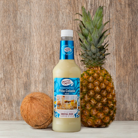 1L bottle of Master Of Mixes Handcrafted Pina Colada Cocktail Mixer next to a coconut and a pineapple.