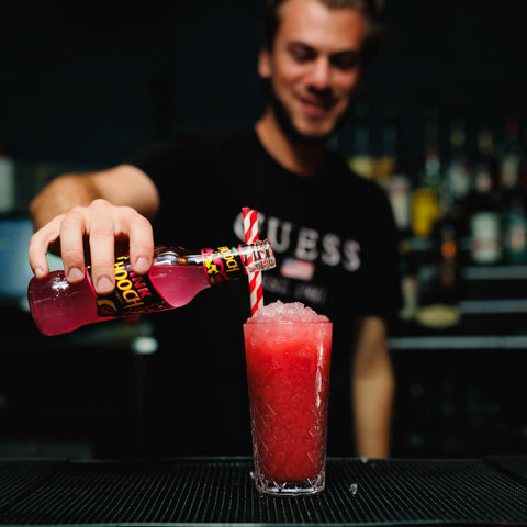 A bartender pouring a vibrant glass of Pink Hooch into a glass full of crushed ice to make a tasty frozen alcoholic drink