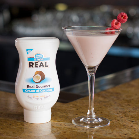 Squeezy bottle of gourmet Cream of Coconut Re'al next to a cocktail garnished with raspberries.