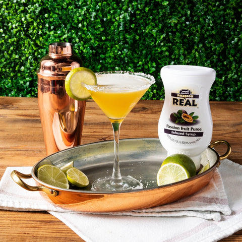 Reàl Passion Fruit Puree Cocktail with lime garnish on a tray next to a bottle of passion fruit puree.