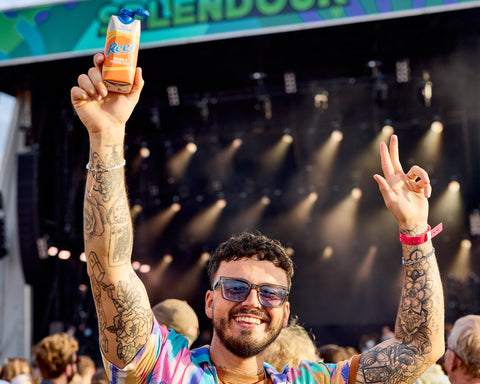 Someone at a festival holding a can of Reef premixed orange and passionfruit drink. 