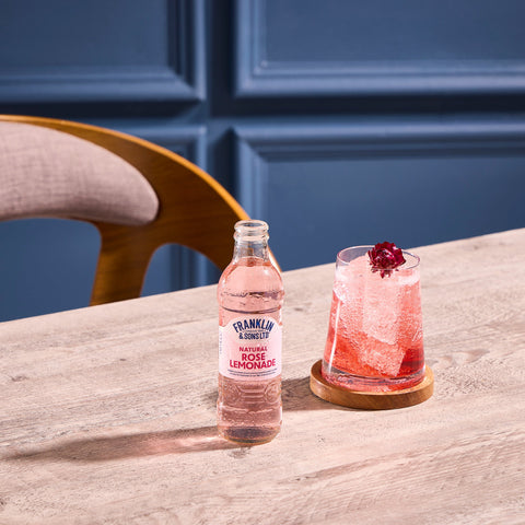 A bottle of Franklin & Sons natural rose lemonade, a premium soft drink with the drink in a glass next to the bottle 
