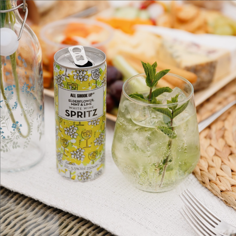 A can of All Shook Up Elderflower and mint white wine spritz cocktail, next to the spritz served in a glass.