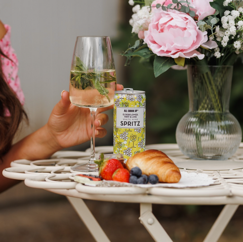 Someone drinking All Shook UP Elderflower, Mint & Lime white wine spritz out of a wine glass with the can on the side. 