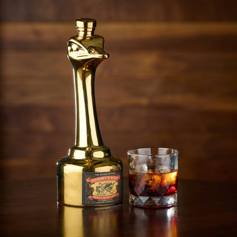 Gold Limited edition ostrich bottle of Shanky's next to a glass of whiskey on a wooden surface