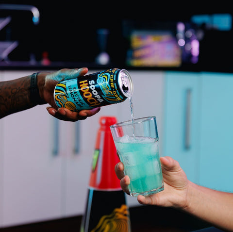 A can of Soopa Hooch Electric Lemonade being poured into a glass with ice making a vibrant delicious drink at a house party.