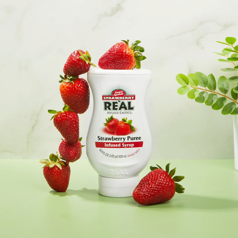 Bottle of Strawberry Reàl Strawberry Puree syrup with strawberries on a light green background