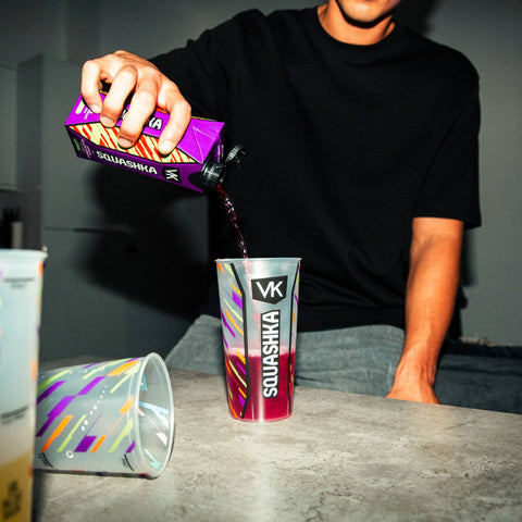 Person pouring a drink from a Squashka box into a colorful cup on a table.