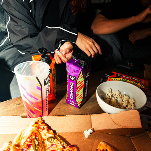 People sitting around a table with pizza, drinks, and snacks.