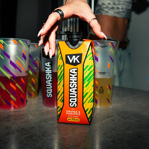 Squashka VK drink container held by a hand with colorful cups in the background