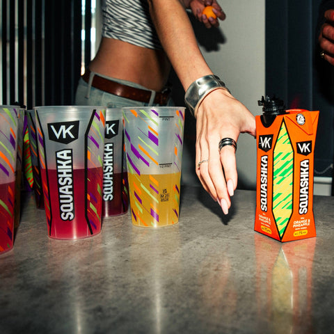 Person reaching for a Squashka drink box on a reflective surface with other Squashka drinks in the background.