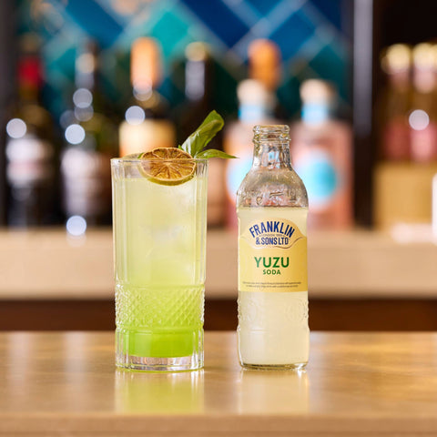 Franklin & Sons Yuzu soda bottle and glass with lime garnish on a bar counter
