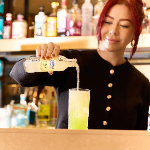 Person pouring Franklin and Sons yuzu soda from a bottle into a glass at a bar.