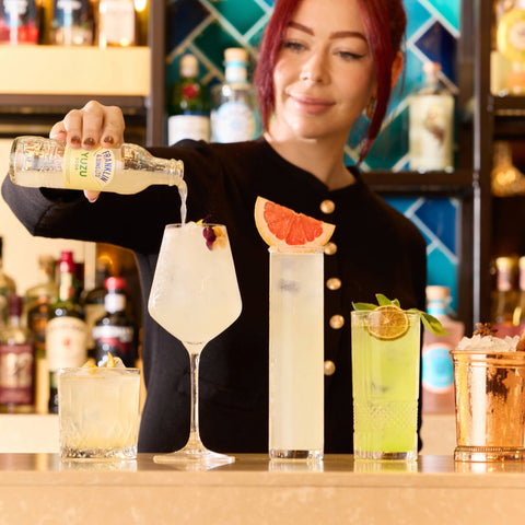 Bartender pouring a Franklins & Sons yuzu soda into a glass with various cocktails on a bar.