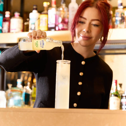 Person pouring a bottle of Franklin & Sons yuzu soda into a glass in a bar setting. 