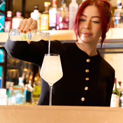 Person pouring a Franklin & Sons into a glass at a bar.