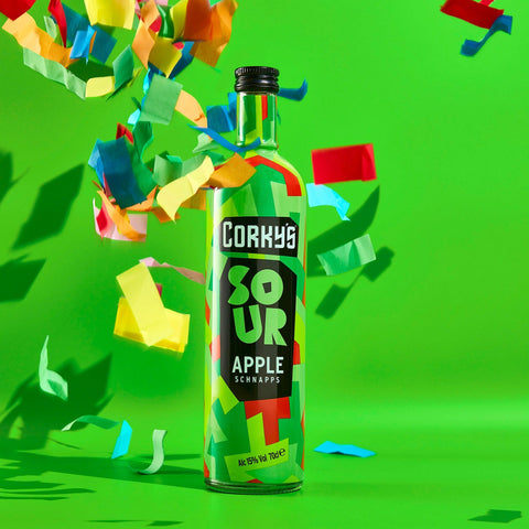 A bottle of Corky's sour apple schnapps on a bright green background with multicoloured confetti. 