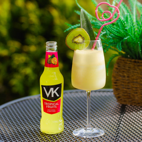 A bottle of VK tropical fruits next to a glass of tropical fruits VK with kiwi garnish. 