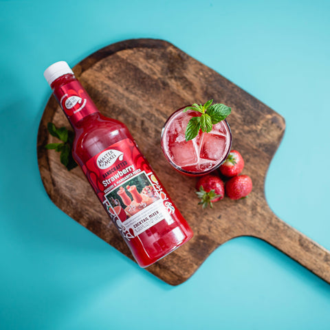 Bottle of Master of Mixes Strawberry on a wooded board next to a drink and strawberries. 