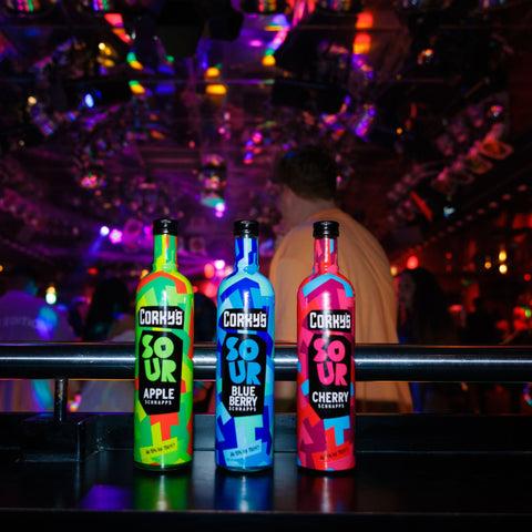 Three bottles of Corky's sour schnapps in flavours: apple, blueberry and cherry lined up on a bar. 