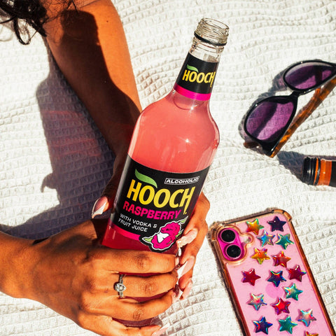 A person holding a big bottle of Hooch Raspberry, an alcoholic pink lemonade, premixed with vodka and fruit juices. 